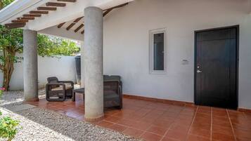 Área de varanda coberta com duas colunas, uma porta e assentos externos.