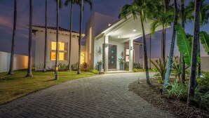 Une maison moderne avec une allée pavée, des palmiers et une entrée bien éclairée.