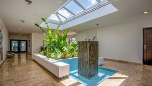 Un vaste espace intérieur avec une verrière, un grand bac à plantes au centre, une piscine et une colonne en bois.