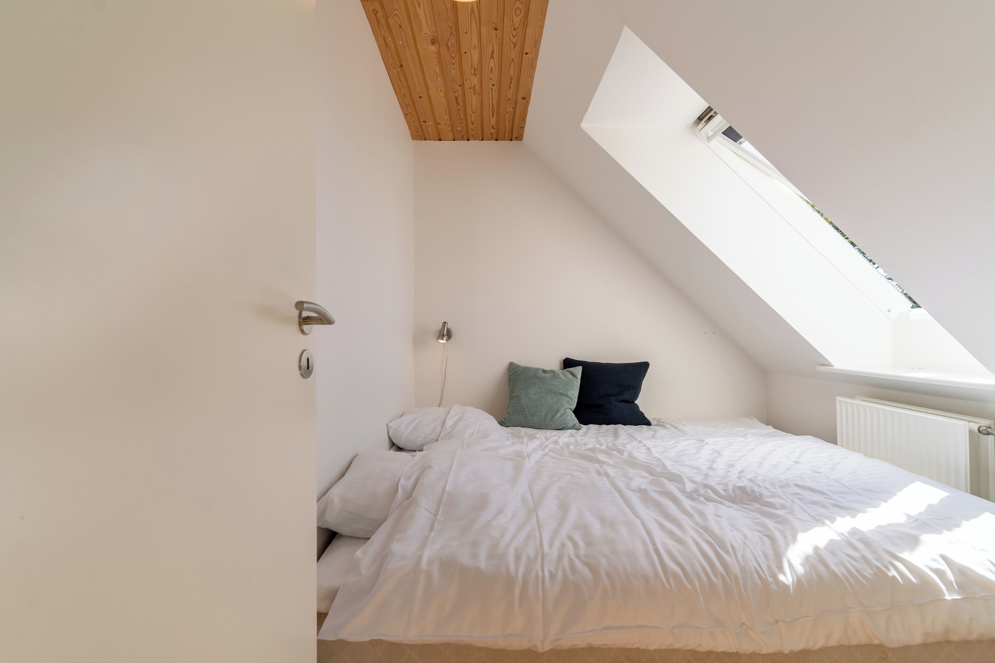 A bedroom with a sloped ceiling, a skylight, a bed with white bedding, and two pillows.