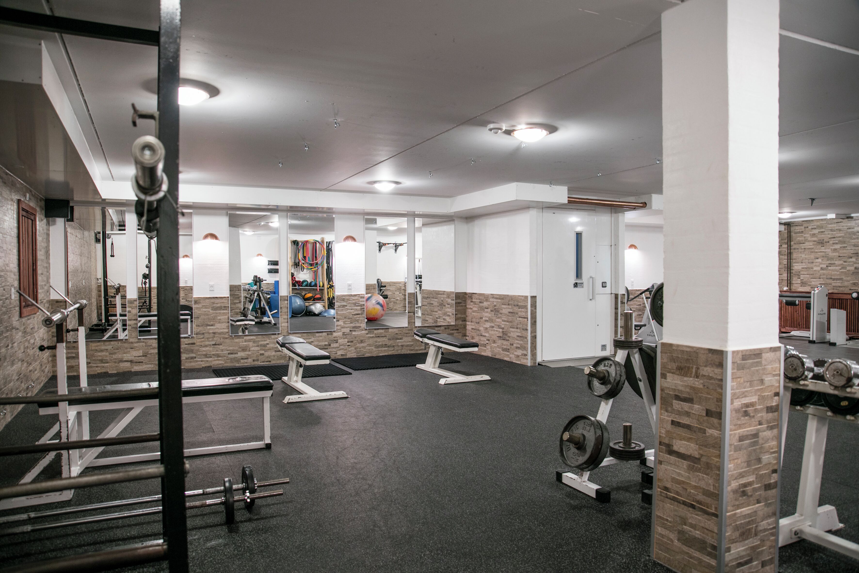 A gym with weightlifting equipment, benches, and a mirrored wall.