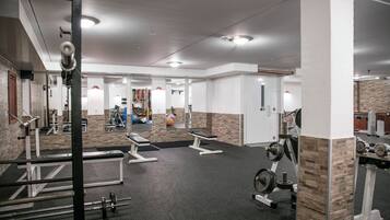 A gym with weightlifting equipment, benches, and a mirrored wall.