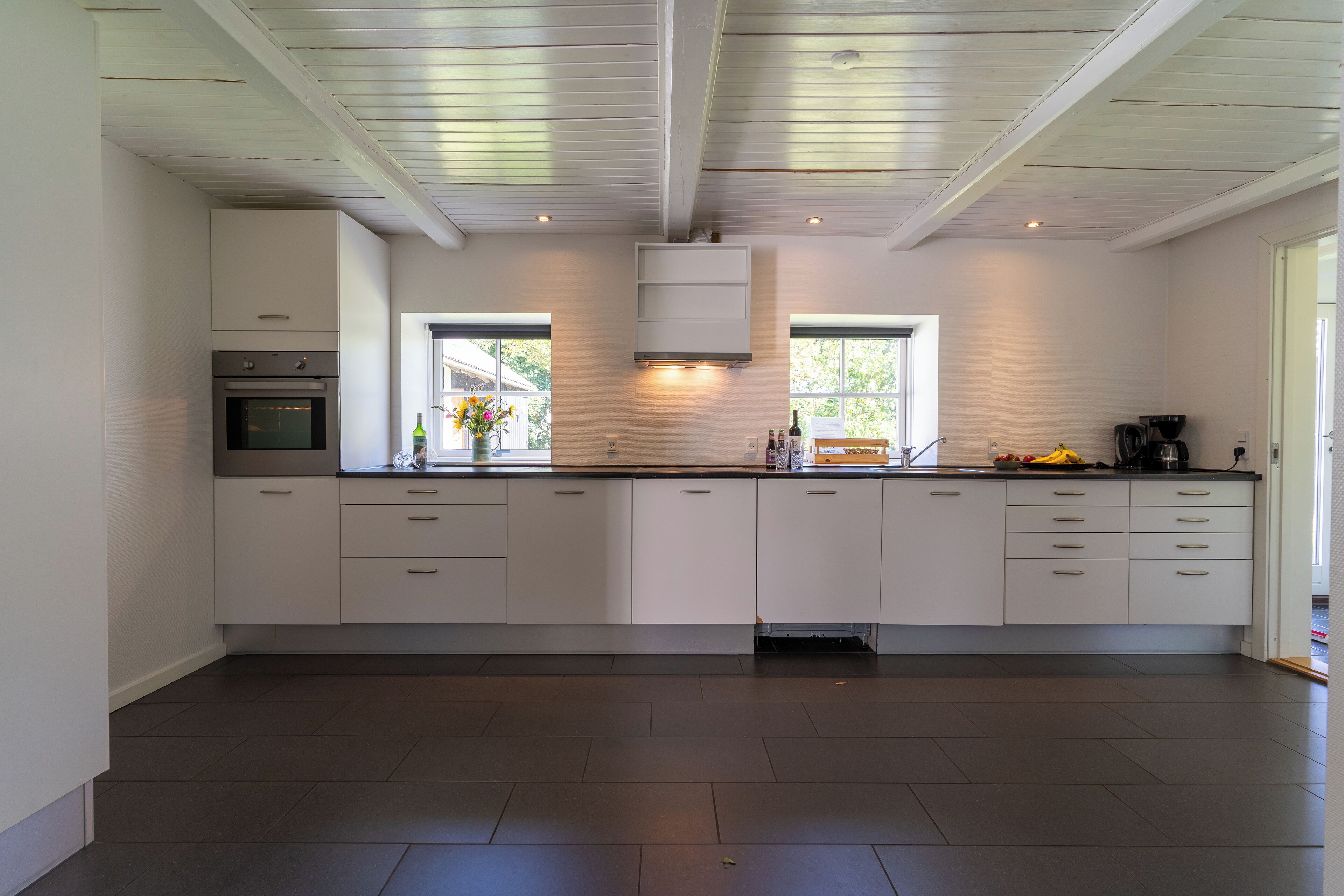 Een moderne keuken met witte kastjes, een ingebouwde oven en een groot raam dat zorgt voor natuurlijk licht.