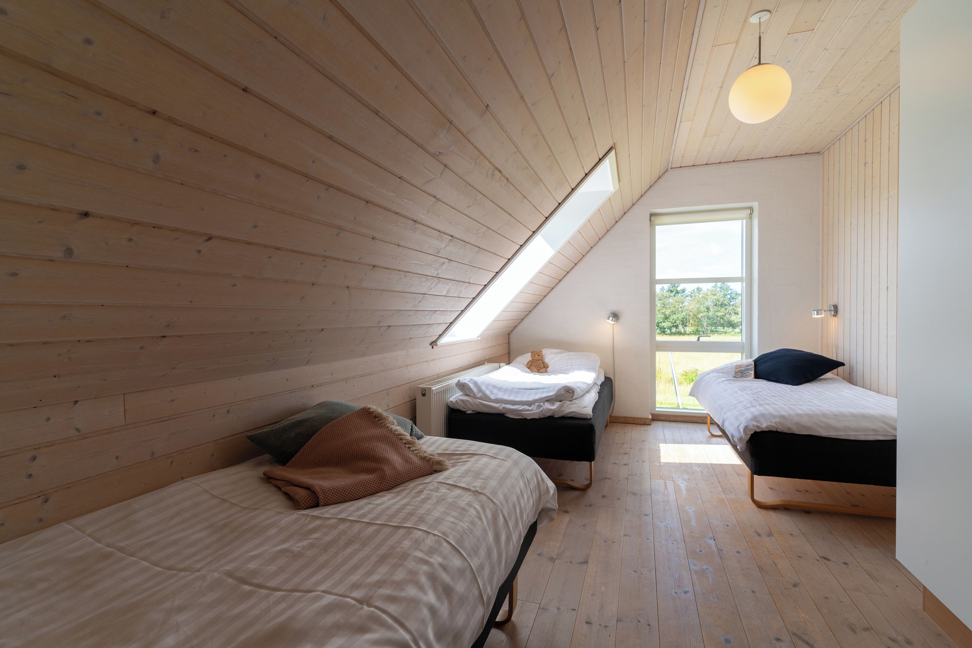 A loft bedroom with two beds, wooden floors, a slanted ceiling, and a skylight.