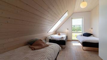 A loft bedroom with two beds, wooden floors, a slanted ceiling, and a skylight.