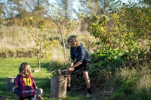 A person chopping wood in a natural setting with a child nearby. - Den Gamle Smedje (Fjerritslev)