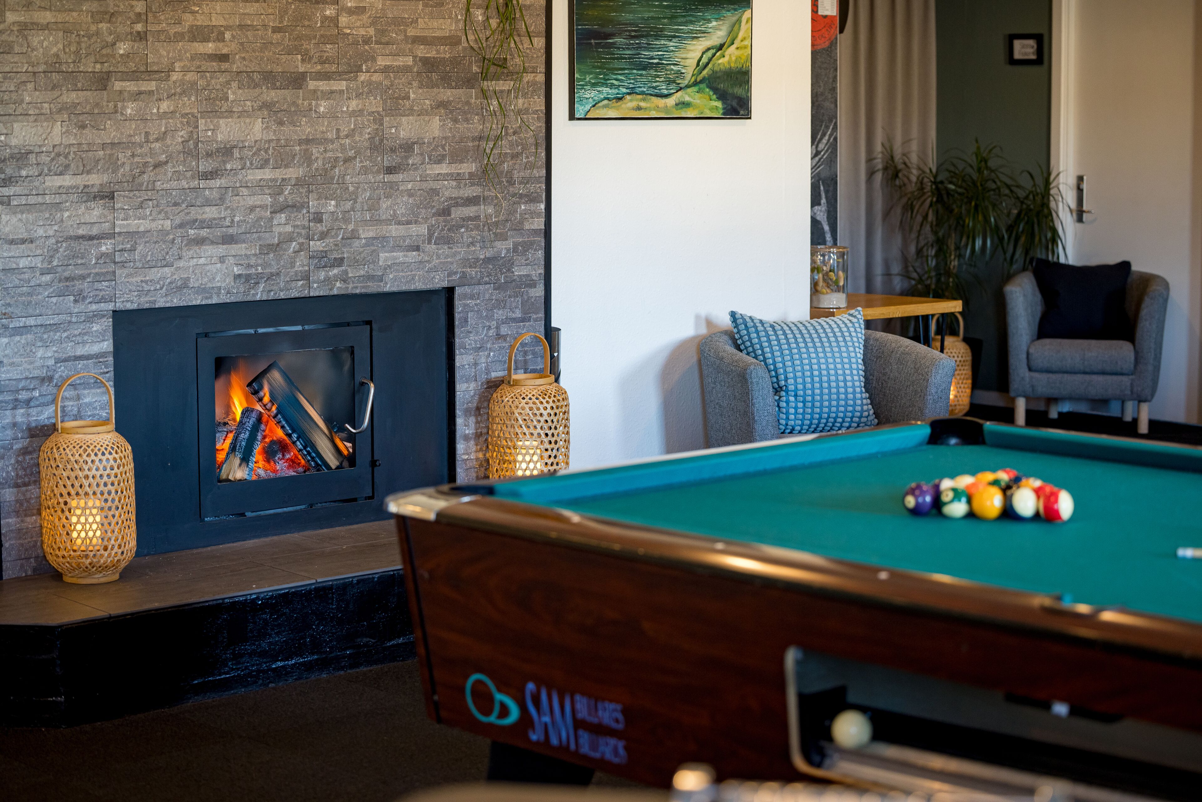 A pool table with balls, a fireplace with logs, and a lounge chair.