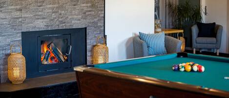 A pool table with balls, a fireplace with logs, and a lounge chair.