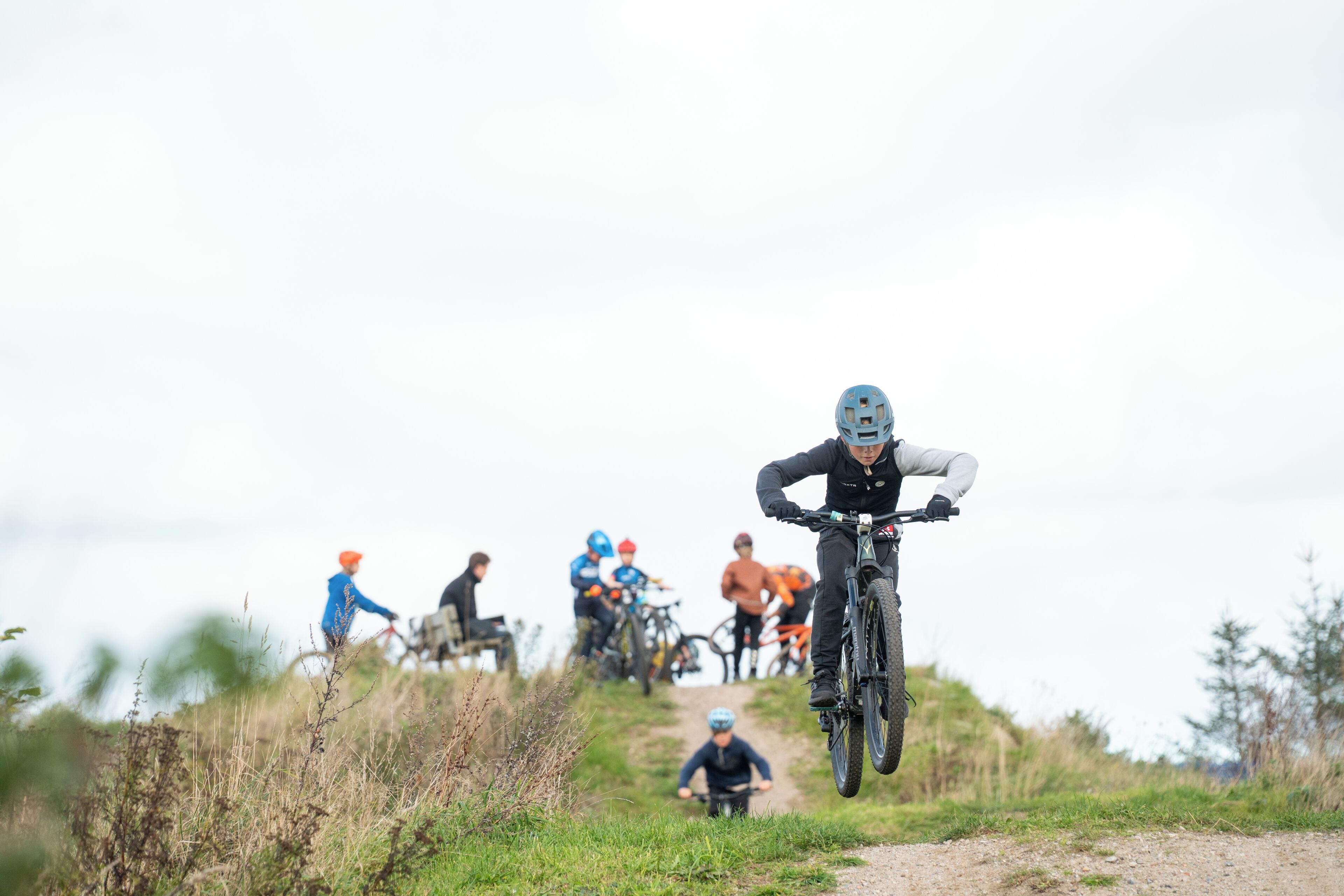 A group of mountain bikers on a dirt trail with a hilly landscape in the background.