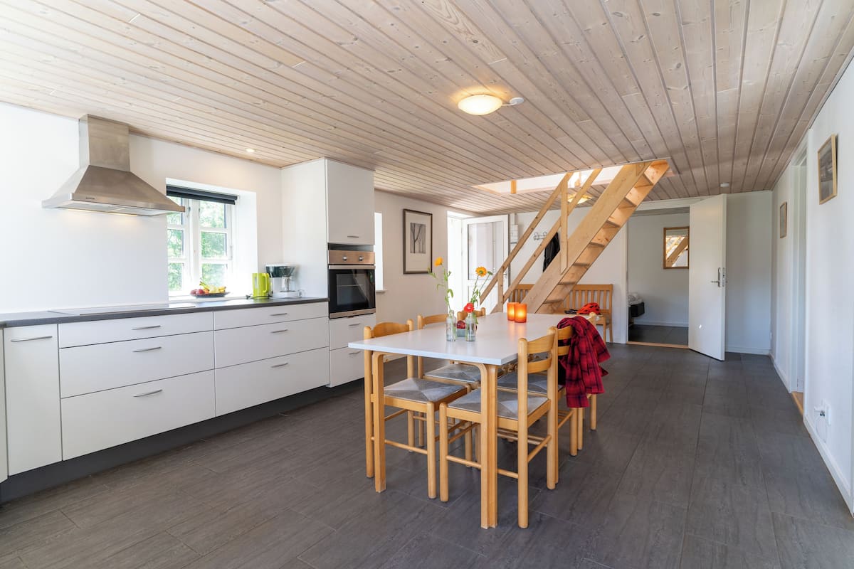 A modern kitchen with white cabinets, a wooden dining table, and a staircase leading to another level.