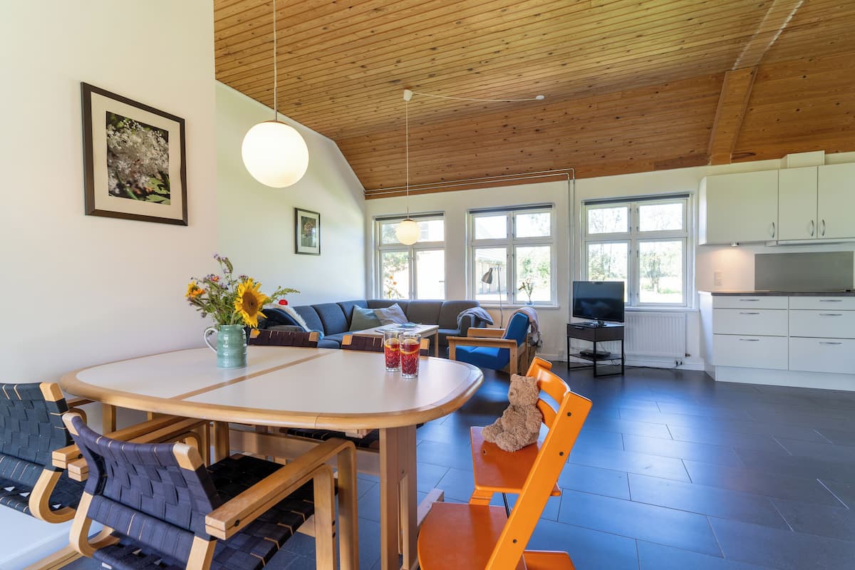 A spacious living area with a wooden ceiling, a round dining table, and a sofa.