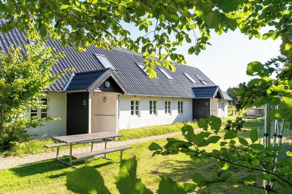 A building with a sloped roof, a wooden bench, and a pathway leading to it. - Den Gamle Smedje (Fjerritslev)