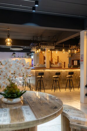 Una zona de bar con mostrador de mármol, taburetes, lámparas colgantes y una planta en maceta.