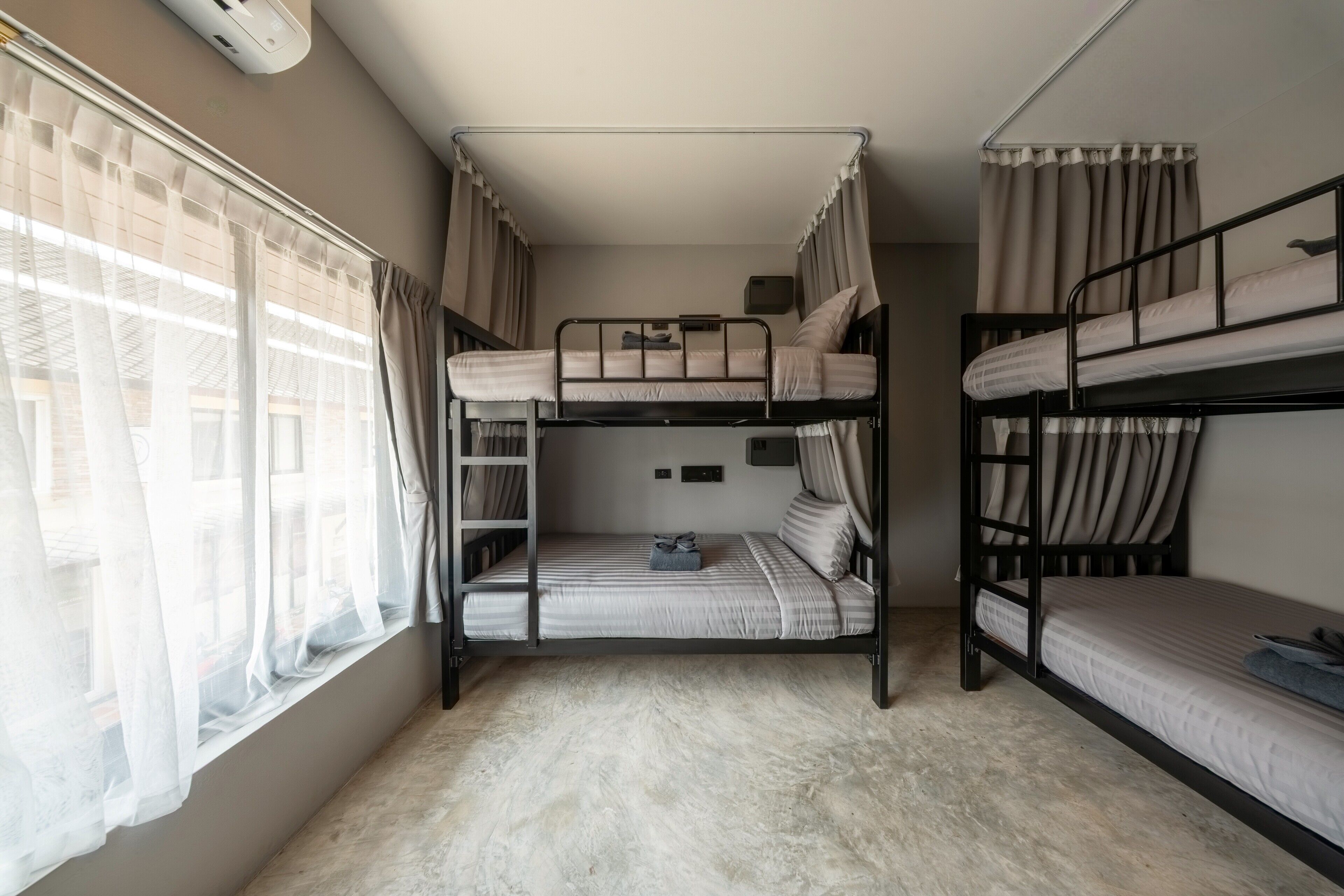 Un dormitorio con literas, una ventana con cortinas translúcidas y un radiador.