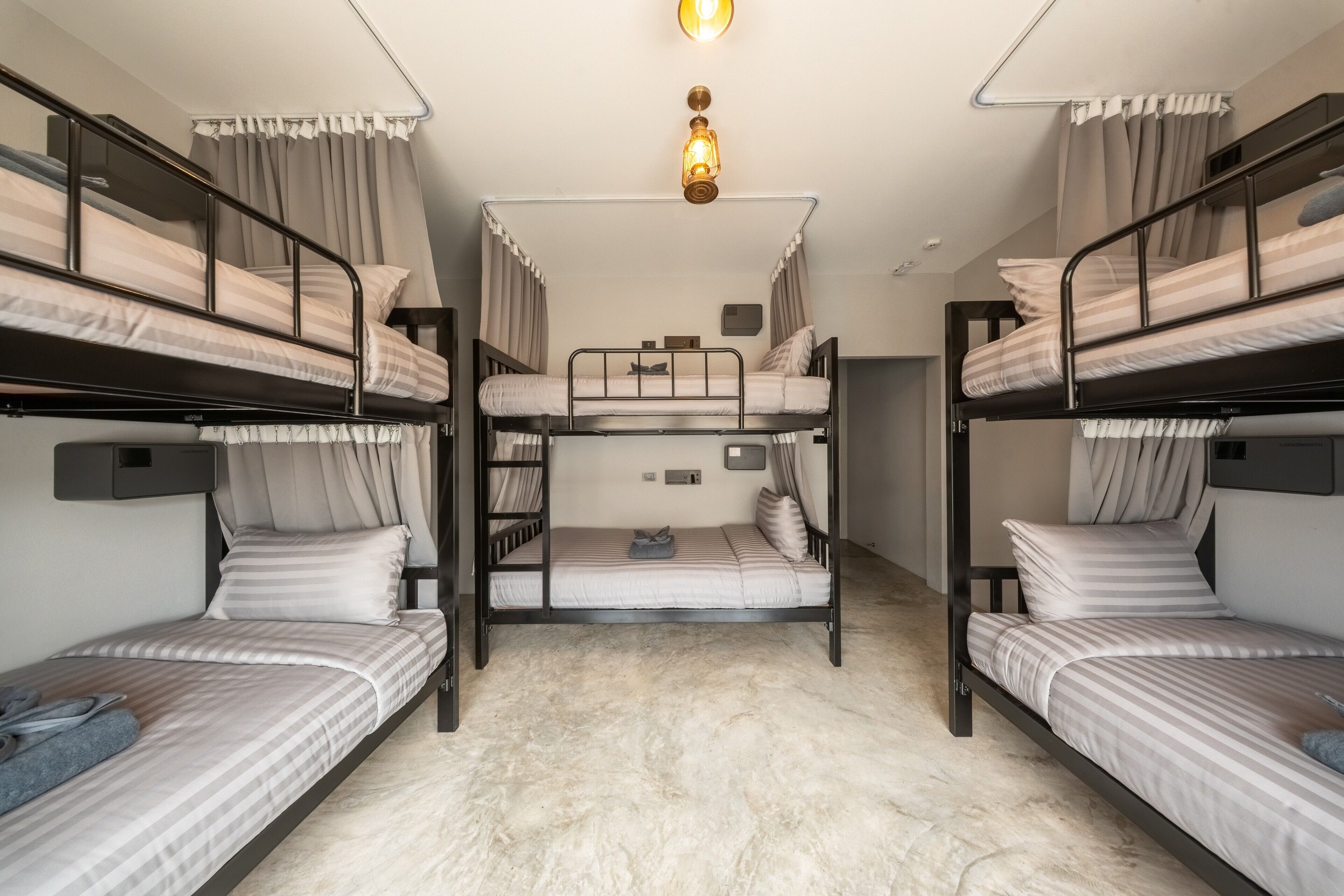 A bunk room with three bunk beds, a ceiling light, and a small bedside table.