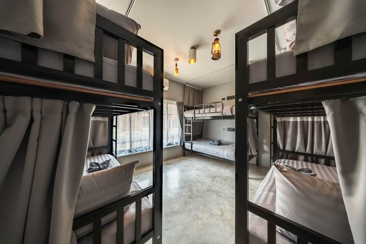 Una habitación con literas, suelo de hormigón y ventana con cortinas.