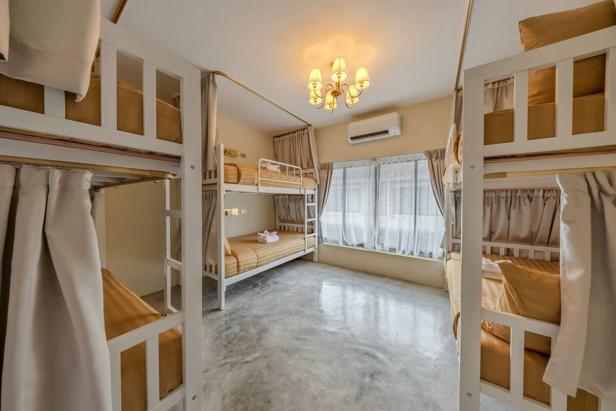 Una habitación con literas, un candelabro, un equipo de aire acondicionado y una ventana con cortinas.