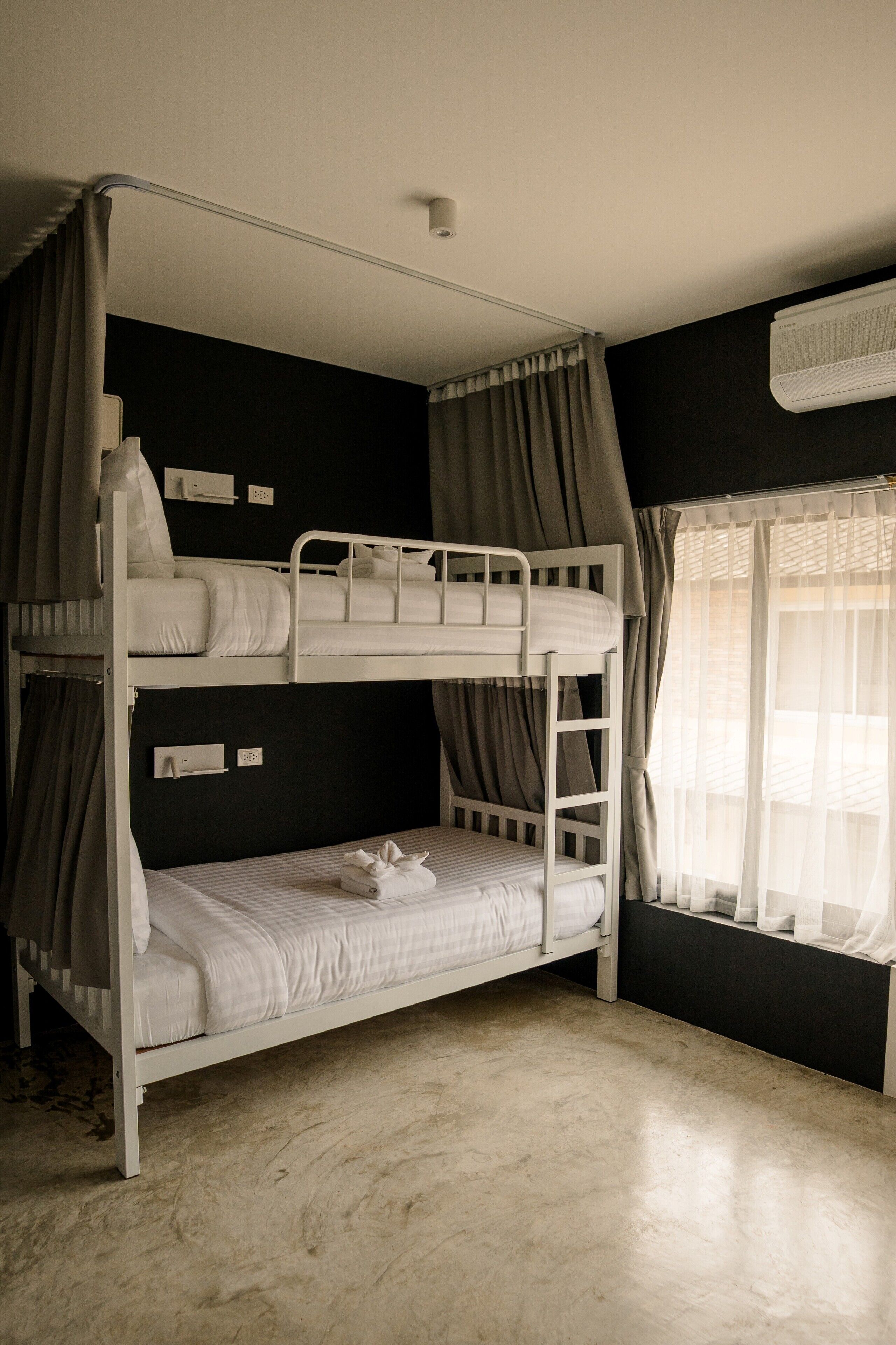 A bunk bed room with a window, curtains, and an air conditioning unit.