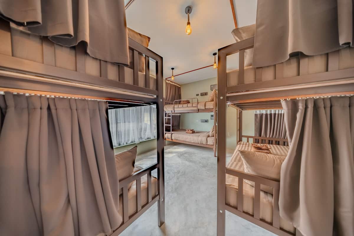 Habitación con literas, cortinas, una lámpara y techo de madera.