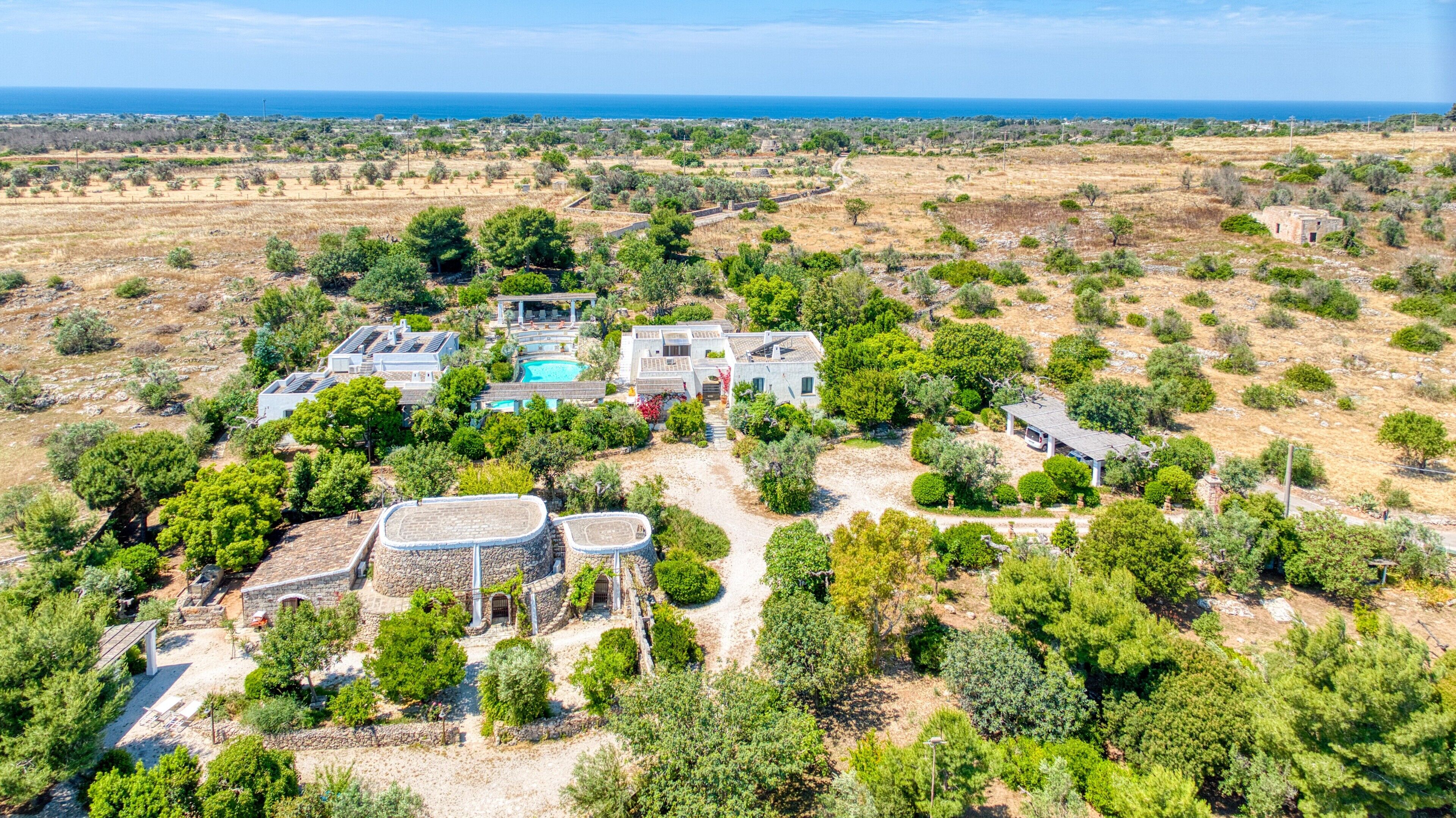 An aerial view of a property with multiple buildings, a swimming pool, and a large stone structure.