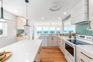 A modern kitchen with a large island, wooden flooring, and a view of the ocean. - Ocean Immersion|Oceanfront·Private Boardwalk·PKS (Pine Knoll Shores)