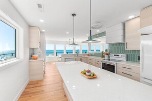 Een moderne keuken met een groot eiland, houten vloeren en uitzicht op zee.