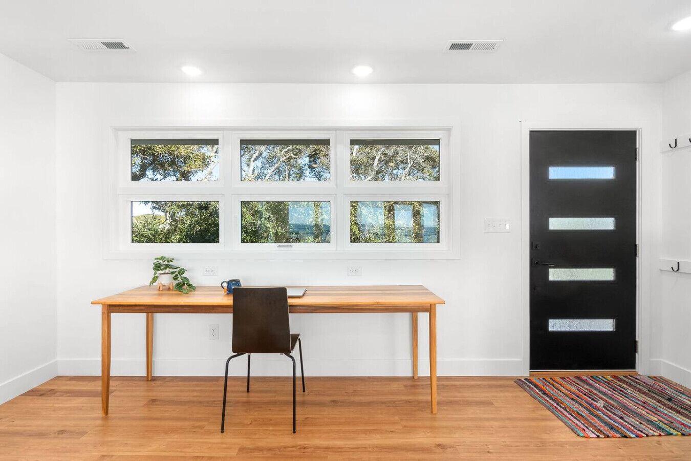 A room with a wooden desk, a chair, a black door, and a window with a view of trees.