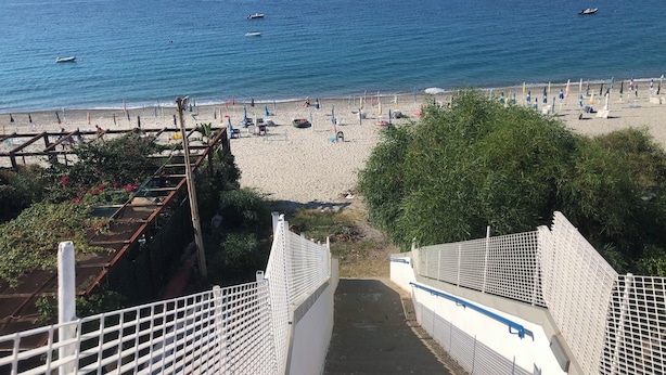 Una playa con vista clara al mar, una orilla arenosa y un camino que lleva a la playa.