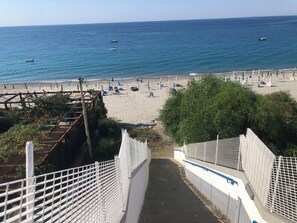 Een strand met helder uitzicht op de zee, een zandstrand en een pad dat naar het strand leidt.