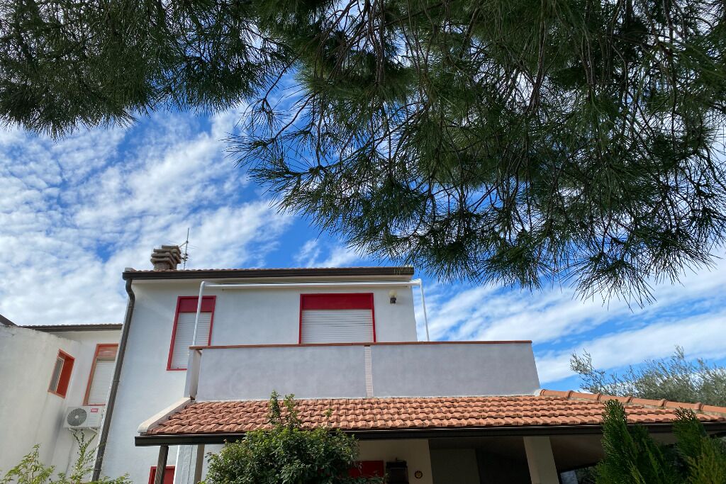 Un bâtiment avec un toit recouvert de tuiles rouges, une façade blanche et une porte rouge.