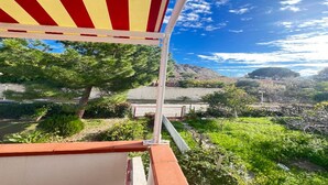 Una terraza con toldo a rayas rojo y amarillo, vista a un viñedo y una montaña al fondo.