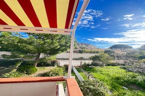 A terrace with a red and yellow striped awning, a view of a vineyard, and a mountain in the background.