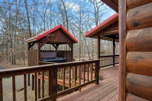 A wooden cabin with a deck and hot tub, surrounded by trees. - Kodiak Bear-hot Tub-playground-location! (Broken Bow)