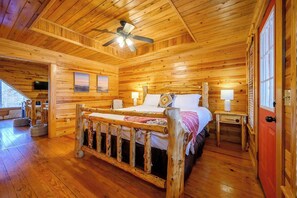 A wooden cabin bedroom with a bed, a nightstand, a ceiling fan, and a window. - Kodiak Bear-hot Tub-playground-location! (Broken Bow)
