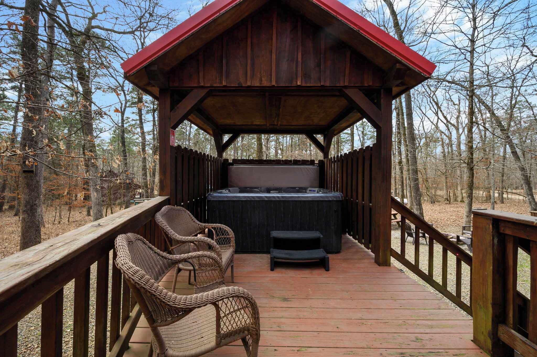 A wooden deck with a hot tub, wicker chairs, and a covered area with a red roof.