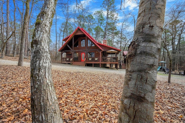 A wooden cabin with a red roof surrounded by trees and fallen leaves.