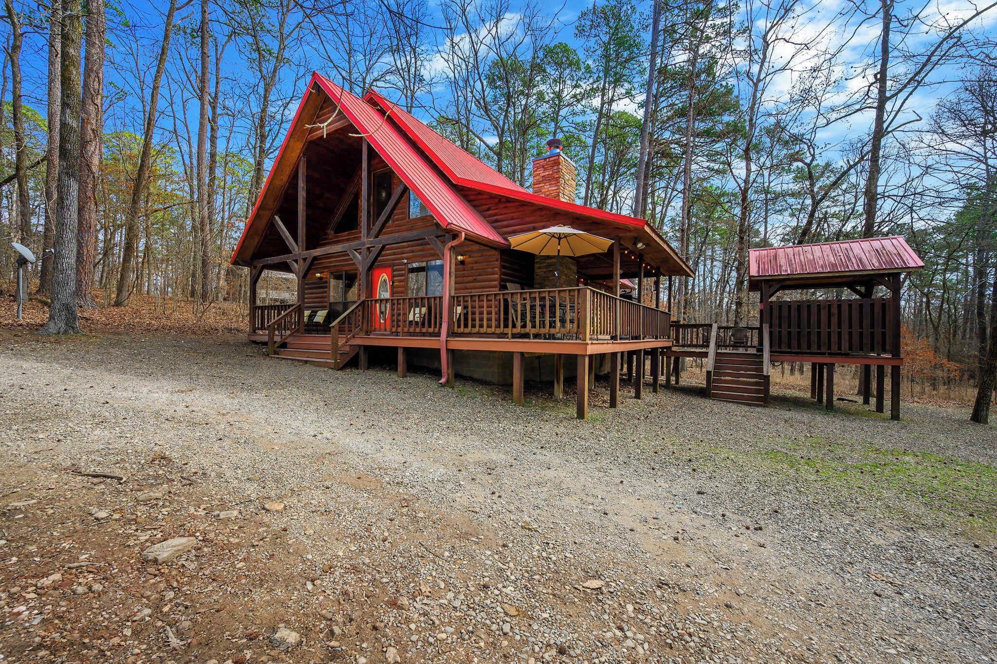 A rustic cabin with a red roof, wooden deck, and a chimney.