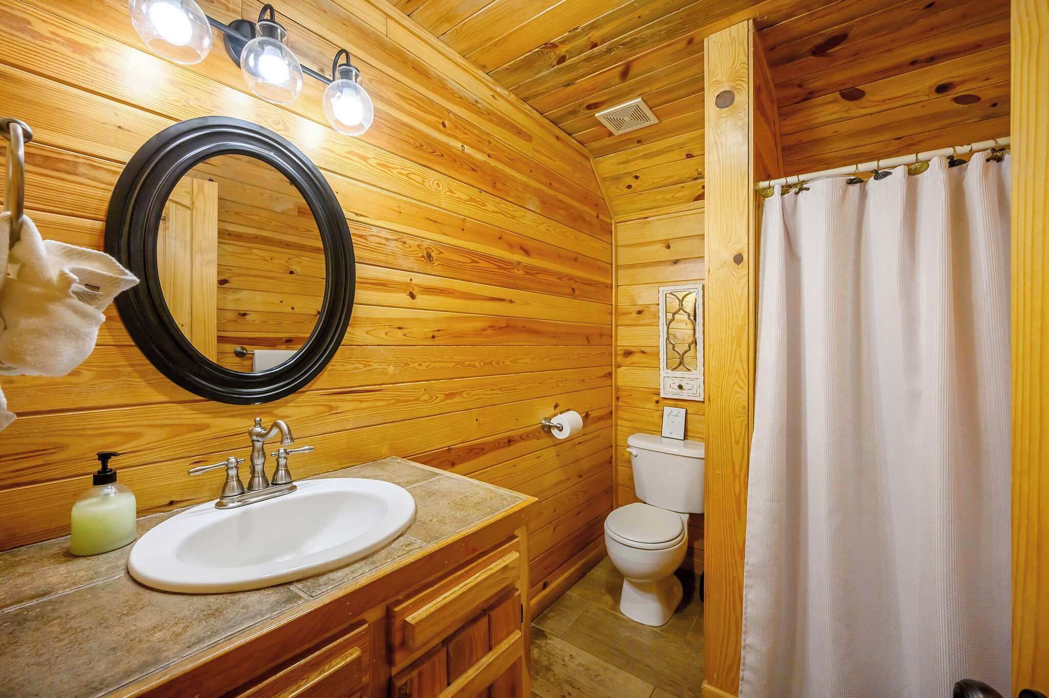 A wooden cabin bathroom with a sink, mirror, and toilet.