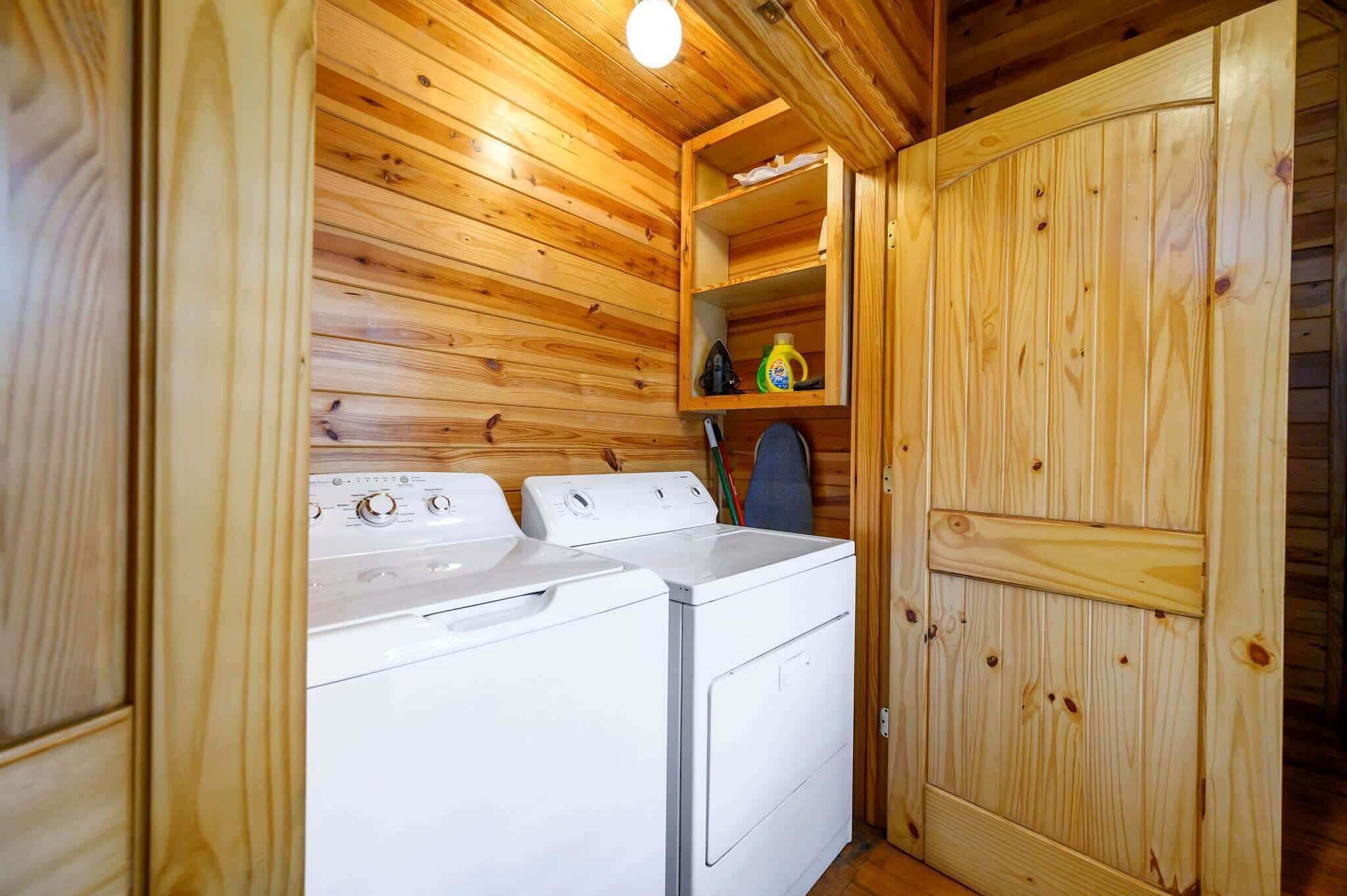 Une buanderie équipée de deux machines à laver et d’un sèche-linge, avec des murs en bois et une étagère contenant des produits de nettoyage.