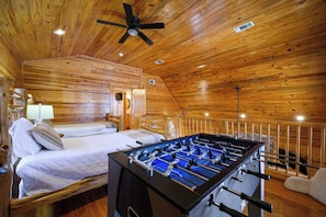 A cozy room with wooden walls, a bed with pillows, a foosball table, and a ceiling fan.