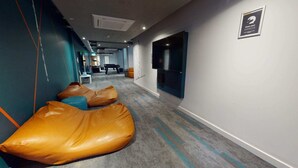 A hotel corridor with bean bags, a TV on the wall, and a 'Clean your hands' sign. - Student Only Elgin Place (Glasgow)