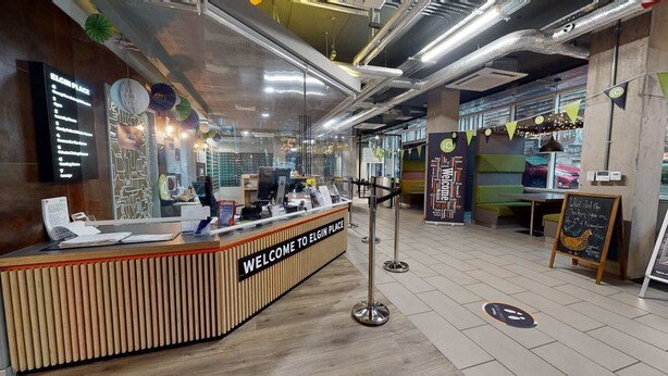 A reception area with a wooden counter, a sign reading "WELCOME TO ELGIN PLACE," and a menu board to the left. - Student Only Elgin Place (Glasgow)