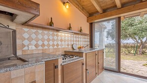 Una cocina con protector de piedra, armarios de madera, estufa a gas y un amplio ventanal con vista a un jardín.