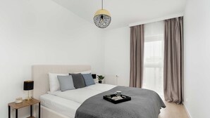 Et moderne soveværelse med seng, natbord, lampe og en dekorativ hængende lysarmatur.
