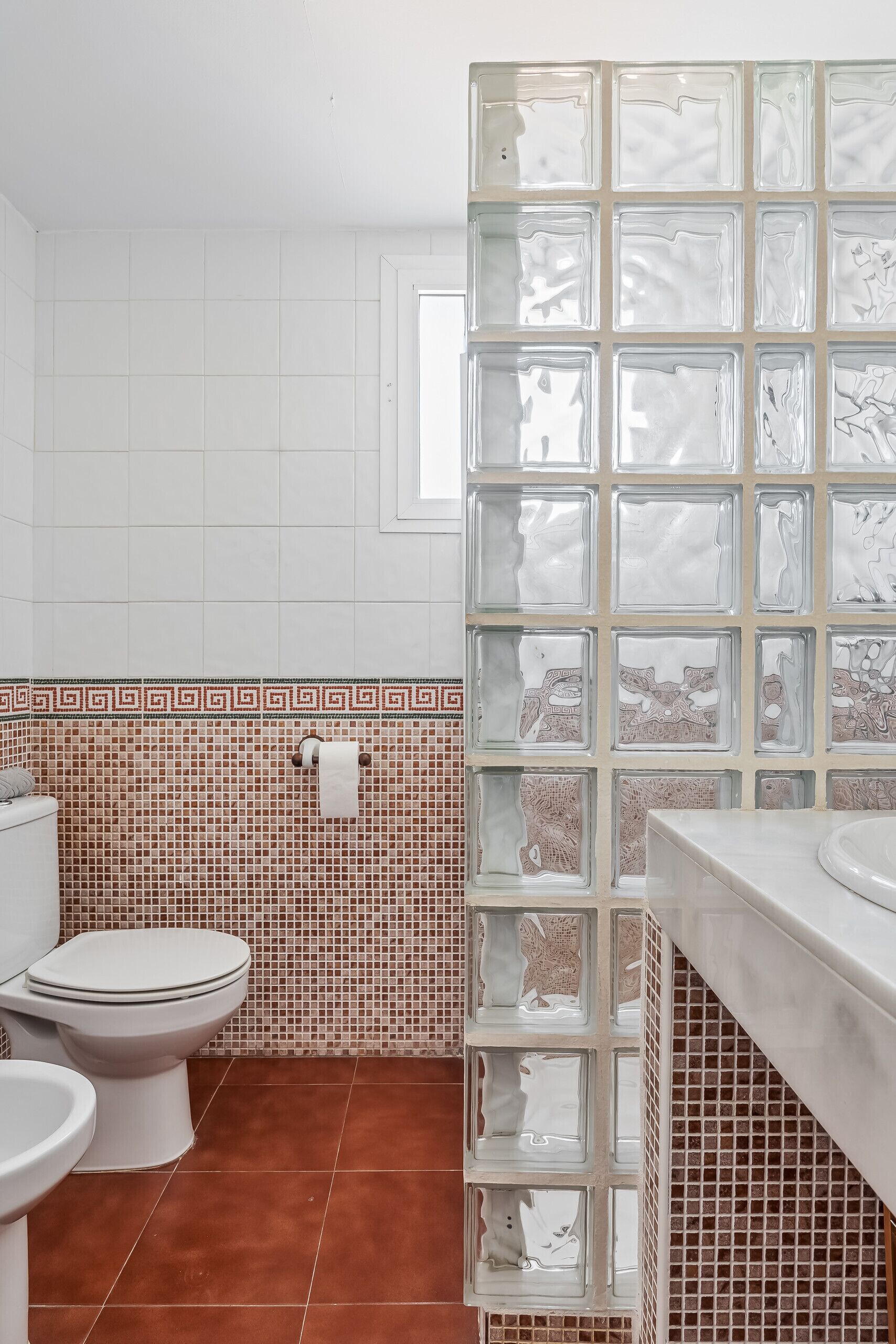 Une salle de bain avec des toilettes blanches, un lavabo et une cloison en verre.