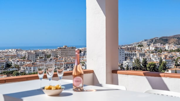 A balcony with a table set for a meal, overlooking a coastal cityscape. - Burriana Beach – 3 Spacious Terraces with Sea Views (Nerja)