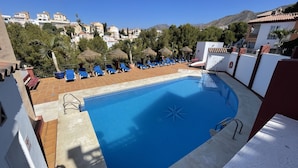 A swimming pool with blue water, surrounded by lounge chairs and umbrellas. - Burriana Beach – 3 Spacious Terraces with Sea Views (Nerja)
