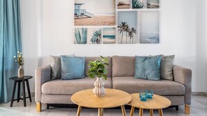 A modern living room with a beige sofa, two round wooden tables, a vase with flowers, and a wall art collage. - Burriana Beach – 3 Spacious Terraces with Sea Views (Nerja)