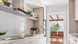 A modern kitchen with white cabinetry, a built-in oven, and a dining area with wooden chairs and a table. - Burriana Beach – 3 Spacious Terraces with Sea Views (Nerja)