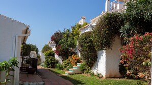 A narrow pathway leading to a white building with a tiled roof, surrounded by lush greenery and flowering plants. - Charming Holiday Apartment in Nerja (Nerja)